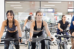 Female Clients Riding Exercise Bikes In Health Club