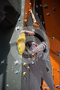 Female climber is climbing up on indoor rock-climbing wall