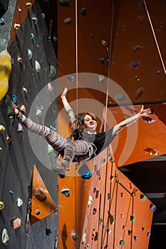 Female climber is climbing up on indoor rock-climbing wall