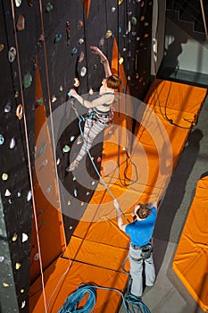 Female climber is climbing up on indoor rock-climbing wall