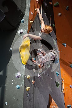 Female climber is climbing up on indoor rock-climbing wall