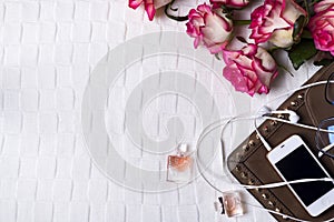 Female clutch with phone, headphones and Perfume bottles with flowers