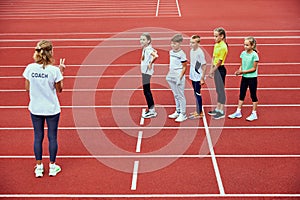 Female coach training athletes. Group of children running on treadmill at the stadium. Concept of sport, achievements