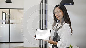 Female coffee shop owner in apron showing digital tablet. Blank screen for advertising text.