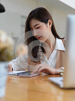 Female college student doing homework with laptop and smartphone