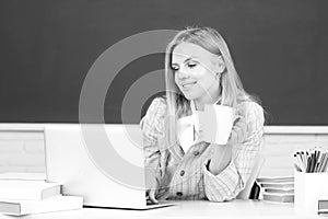 Female college student drinking coffee or tea, working on a laptop in classroom, preparing for an exam.