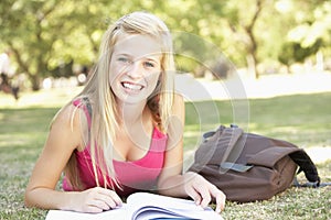 Female College Student Lying In Park Reading Textbook