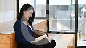 Female college student reading a book in the library.