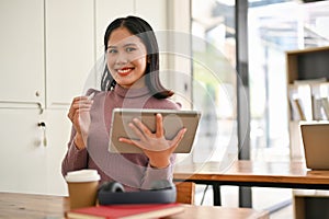 A female college student sits in a campus co-working space with a tablet in her hand