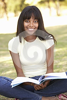 Female College Student Sitting In Park Reading Textbook