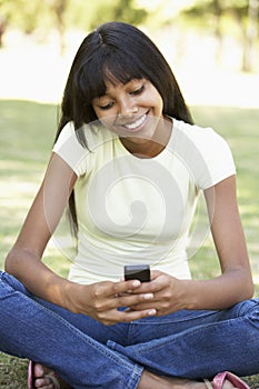 Female College Student Sitting In Park Using Mobile Phone