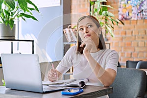 Female college student studying using laptop, sitting in coworking cafe