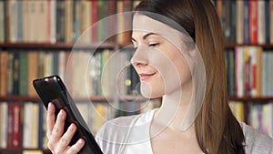 Female college student using e-book in university library. Bookcase bookshelves in the background