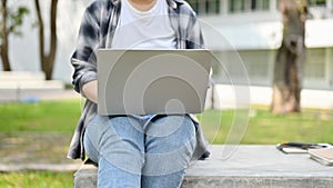 A female college student using her laptop on a bench in the campus park