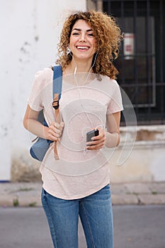 Female college student walking outside with mobile phone and earphones