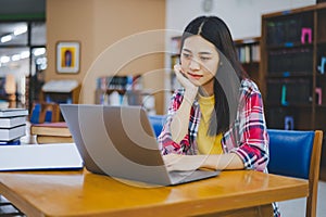 Female college student working on laptop and searching for books to study, make report, find useful information in college room.