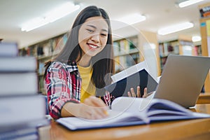 Female college student working on laptop and searching for books to study, make report, find useful information in college room.