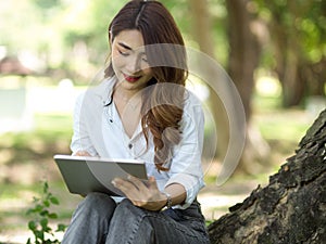 A female college student works on her assignment using a tablet computer in a city park