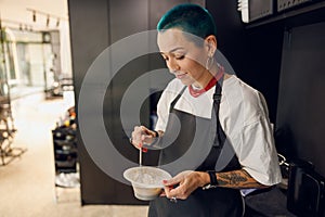 Female colorist preparing a hair dye in a container while working in beauty salon