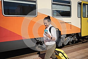 Female commuter harrying up to board train, checking her mobile phone while walking along the railway station platform