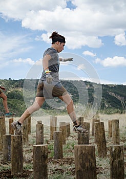 Female competitor running across tall wooden stumps
