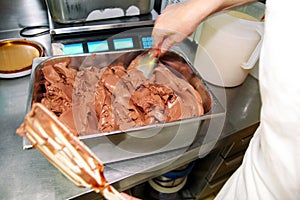 Female confectioner in chef uniform is working at ice cream factory. Woman is decorations of black chocolate ice cream flavors.