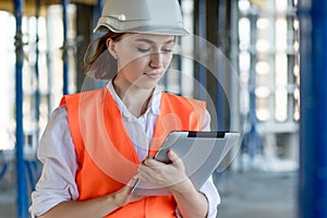 Female construction engineer. Architect with a tablet computer at a construction site. Young Woman looking, building