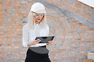 Female construction engineer. Architect with a tablet computer at a construction site. Young Woman looking, building