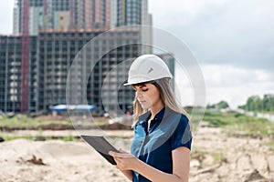 Female construction engineer. Architect with a tablet computer at a construction site. Young Woman looking, building