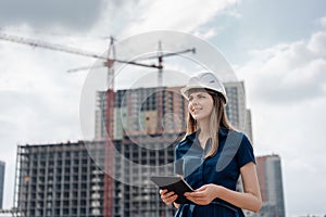 Female construction engineer. Architect with a tablet computer at a construction site. Young Woman looking, building