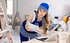 Female contractor in blue uniform using laptop at construction site