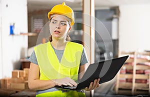 Female contractor using laptop to check plan of building under construction