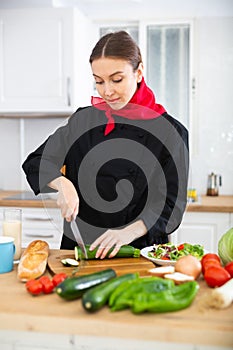 Female cook in black uniform chopping vegetables in kitchen