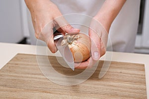 female cook cuts onions on a wooden board in a white apron in her kitchen