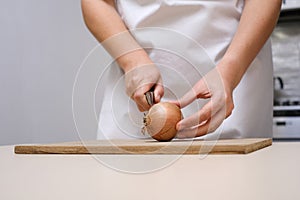female cook cuts onions on a wooden board in a white apron in her kitchen