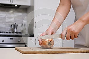 female cook cuts onions on a wooden board in a white apron in her kitchen