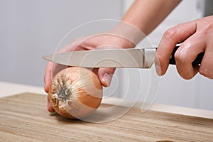 female cook cuts onions on a wooden board in a white apron in her kitchen