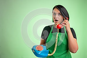 Female cook with green apron and black t-shirt looking surprised while talking on an old phone