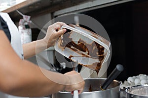 Female cook hands introducing chocolate into bowl for preparing sweet cake