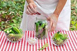 Female cook puts red pepper in a glass jar with cucumbers for preservation