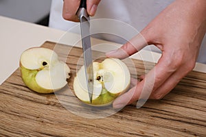 female cook slices an apple on a wooden board in her kitchen