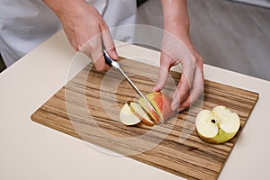 female cook slices an apple on a wooden board in her kitchen