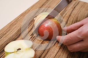 female cook slices an apple on a wooden board in her kitchen