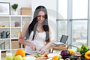 Female cook slicing green cucumber, cooking fresh vegetable salad on cutting board at her kitchen worktop.