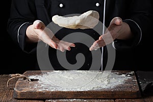 A female cook throws a yeast dough in her hands on a black background