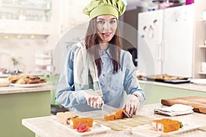 Female cook wearing Chef s hat and gloves making Japanese sushi rolls, smiling, looking at camera in the kitchen