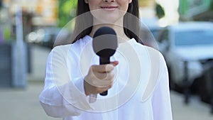 Female correspondent holding microphone outdoors, interview questions, opinion