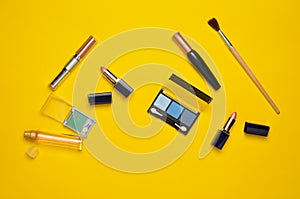 Female cosmetics for make-up layout on a yellow background. Cosmetic shadows, make-up brush, eyeshadow lipstick, perfume bottle.