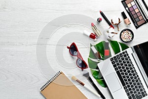 Female cosmetics on white office desk. Laptop, notepad, Lipstick, powder, comb, women`s jewelry. Top view.
