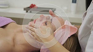 The female cosmetologist anoint the face of lady with the purifying mask in the SPA-salon.